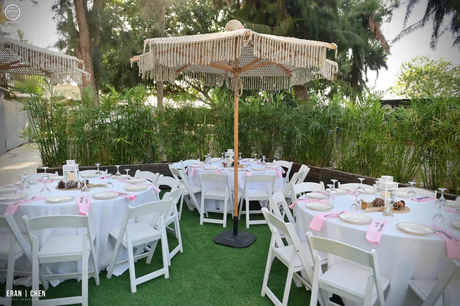 שולחנות עגולים ערוכים בלבן תחת שמשייה על המדשאה